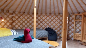 Interior acogedor de una yurta con dos camas, un peluche y un armario de madera.