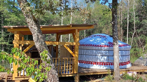 Una yurtas con estructura de madera adosada, rodeada de árboles.