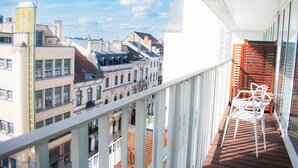 A balcony with a view of historic buildings, a wooden railing, and a white chair.