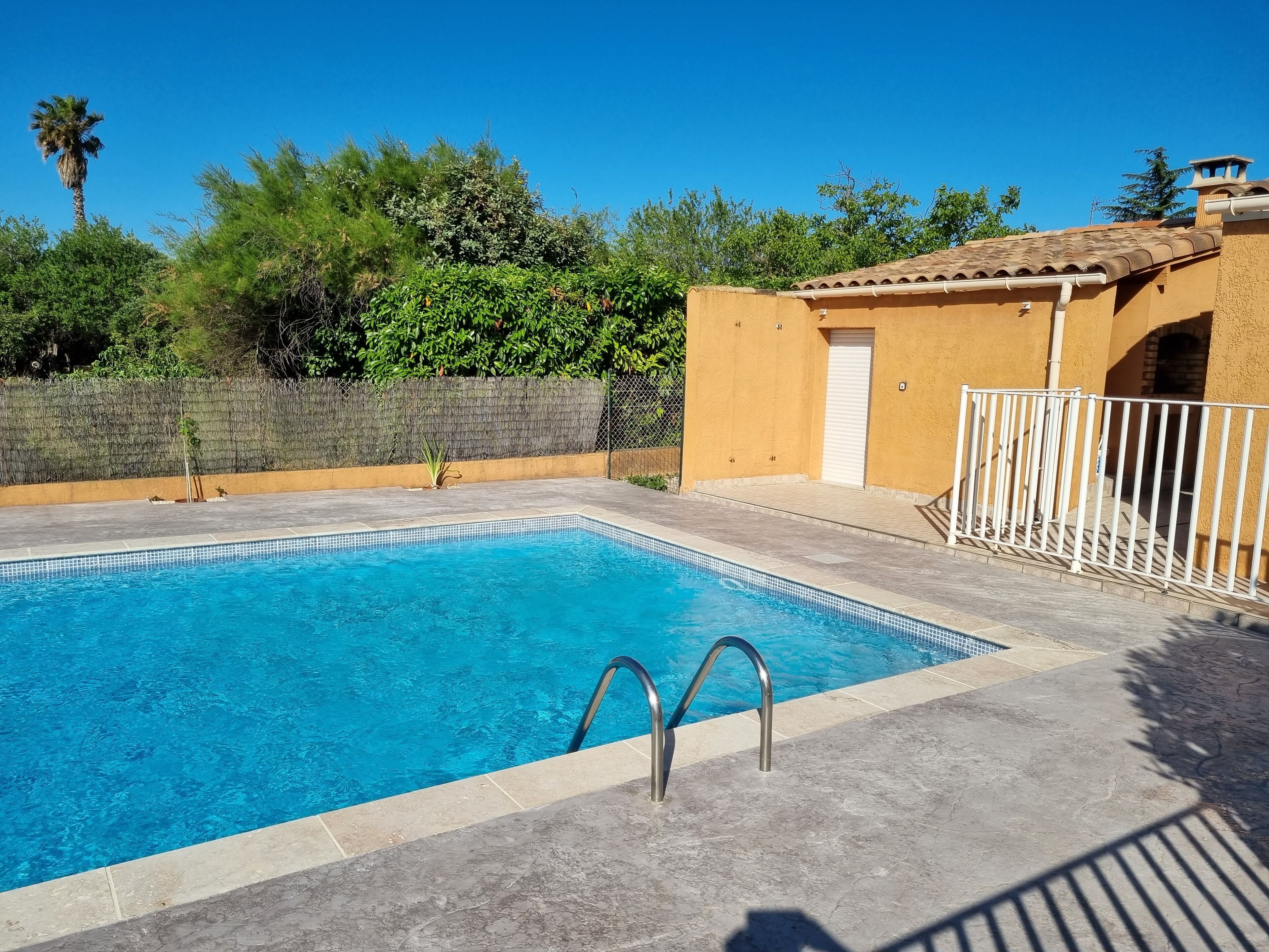 Une piscine avec un bord carrelé, un escalier en métal et une clôture blanche.