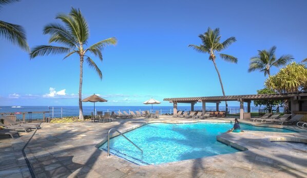 Relax by the oceanfront pool surrounded by palm trees and lounge chairs.