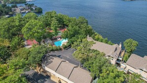 Vista aerea di una proprietà sul lago con piscina, circondata da alberi fitti e diverse case.