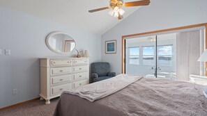 Un dormitorio con cama, cómoda, silla y vista a un cuerpo de agua a través de una puerta corredera.