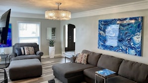 A modern living room with a sectional sofa, a grey armchair, and a large abstract painting. - NEW REMODEL! ARCADE GAMES, PNG PNG, SKEE BALL, ACCESS TO POOL. WE HAVE IT ALL! (Urbandale)