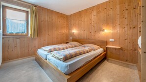 Une pièce aux murs lambrés, avec un lit, une fenêtre avec des rideaux et un luminaire fixé au mur.