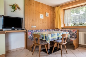 A wooden-paneled room with a television, a table with a floral tablecloth, and a bench.