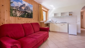 Un canapé rouge dans une pièce comprenant un coin cuisine, des murs en bois et un tableau représentant un paysage de montagne.