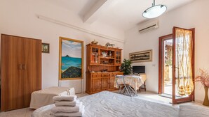 Un dormitorio con cama, un aparador de madera, un escritorio con silla, un cuadro y una puerta que da a un área exterior.