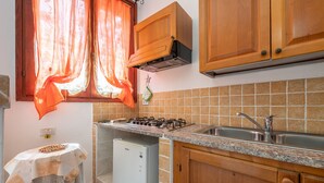Una cocina con estufa a gas, lavamanos, armarios de madera y un refrigerador pequeño.