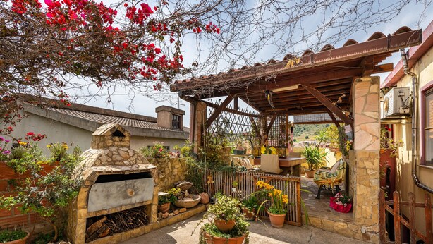 Un horno de piedra, plantas en macetas y una pérgola de madera en un patio.