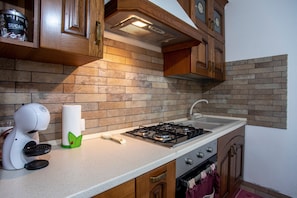 A kitchen with a gas stove, wooden cabinets, a brick backsplash, and a white countertop.