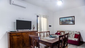 Un comedor con una mesa y sillas de madera, un televisor sobre un mueble de madera y un sofá estampado con motivos florales.