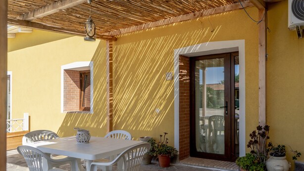 Un patio con una mesa y sillas, plantas en macetas y una puerta que da a un espacio interior.