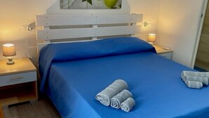Una cama con una colcha azul, dos toallas enrolladas y un cuadro en la pared de velas verdes.