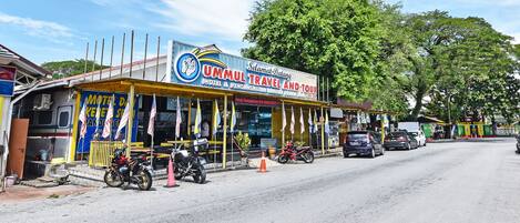 Un'agenzia di viaggi chiamata "UMMUL TRAVEL AND TOUR", con un cartello pubblicitario, una motocicletta parcheggiata di fronte e una strada con veicoli.