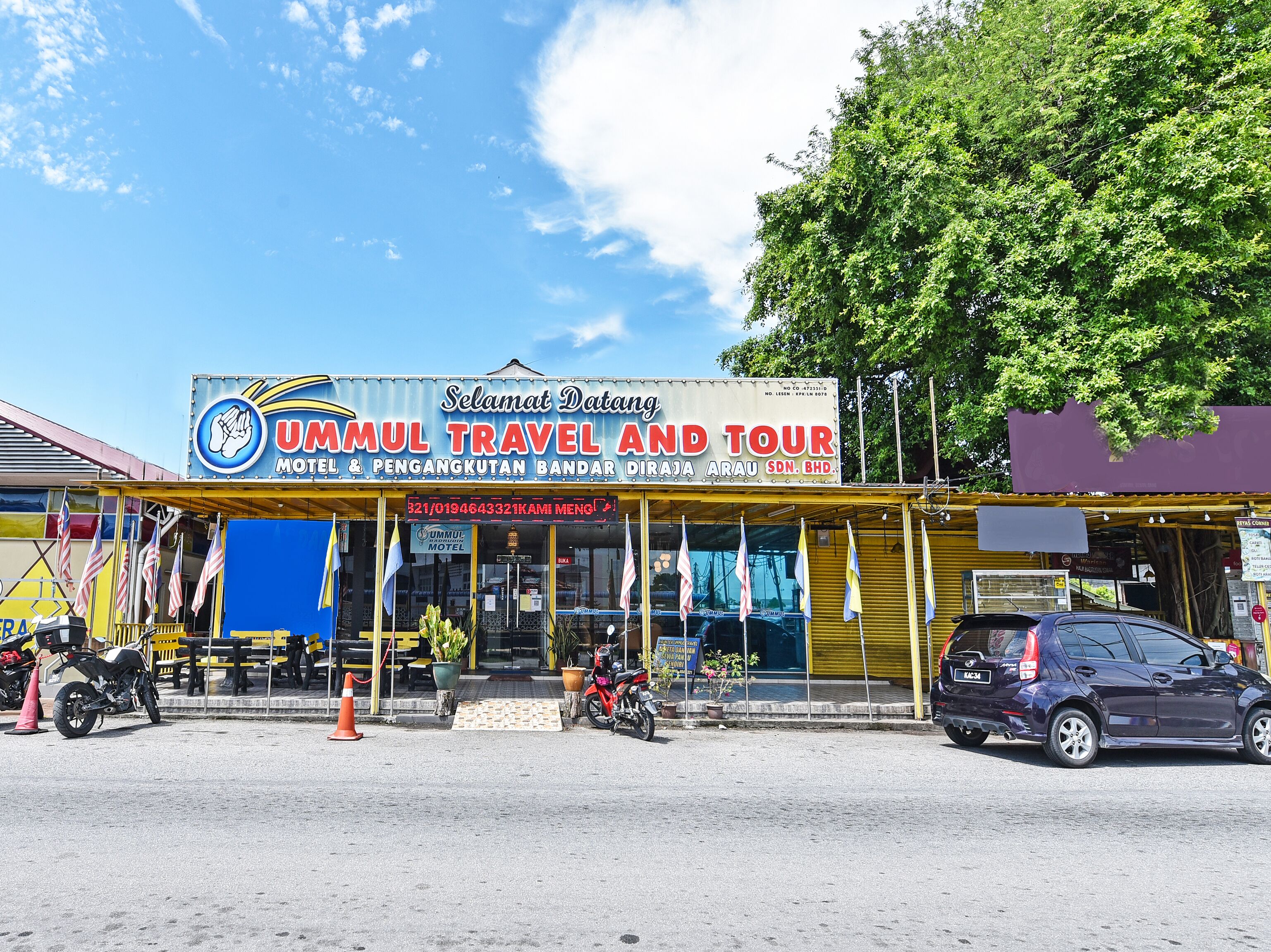 A travel and tour agency named 'UMMUL TRAVEL AND TOUR' with a signboard, a yellow awning, and a blue and white logo.