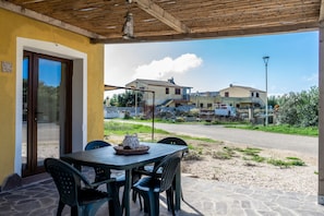 Un patio al aire libre con una mesa y sillas, techo de madera y vistas a casas en el fondo.