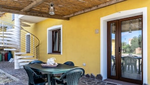 Une terrasse avec une table et des chaises, un escalier en colimaçon et un mur jaune.