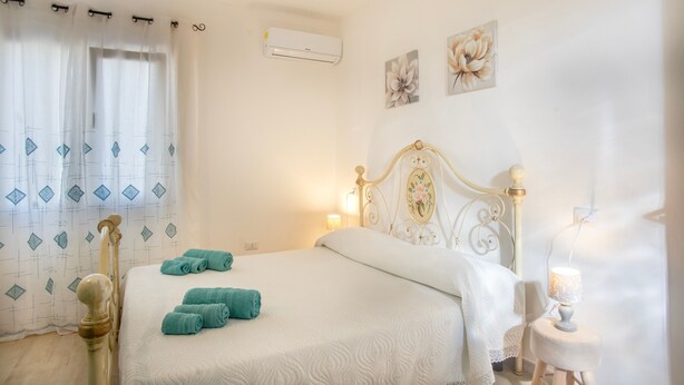Une chambre à coucher avec un lit, une table de chevet avec une lampe, un climatiseur fixé au mur et une fenêtre avec des rideaux.