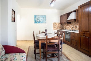 A dining area with a wooden table and chairs, a kitchen with wooden cabinets, and a tiled backsplash.