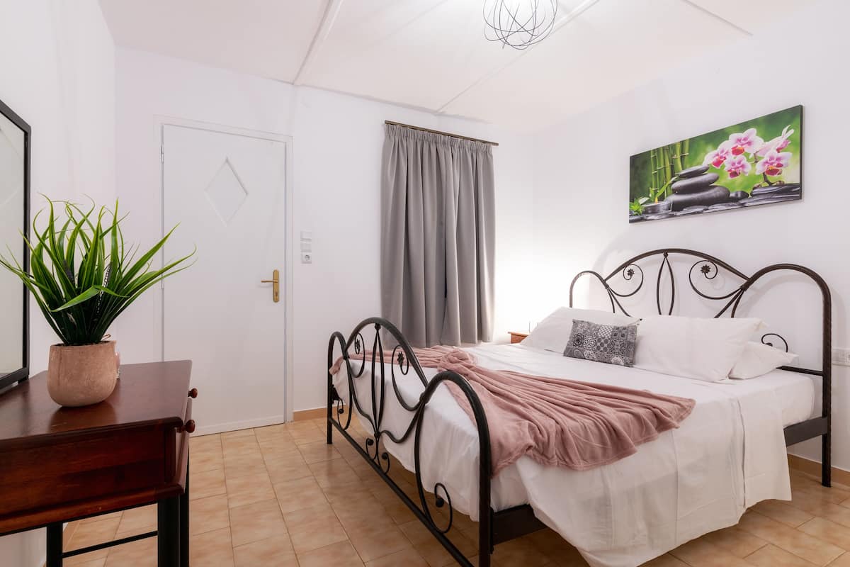 A bedroom with a bed, a potted plant, a painting, and a door.