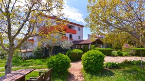 A garden pathway leading to a building with a red roof and white walls, surrounded by lush greenery and a wooden bench. - Apartment 2155/53610 (Istria - Liznjan), 1700m from the beach (Liznjan)