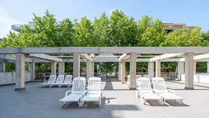 A rooftop terrace with white lounge chairs, a pergola structure, and a view of trees and buildings. - Apartment 'Apartamentos Salou - 112' with Shared Pool, Wi-Fi and Air Conditioning (Salou)