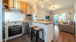 A modern kitchen with a built-in oven, a microwave, and a coffee machine. There is a wooden bar counter with stools, and a sofa in the living area. - Apartment 'Apartamentos Salou - 112' with Shared Pool, Wi-Fi and Air Conditioning (Salou)
