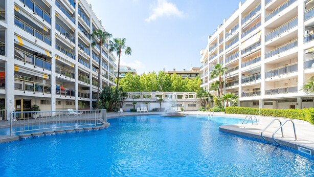 A swimming pool surrounded by multi-story buildings with balconies, a small waterfall feature, and greenery. - Apartment 'Apartamentos Salou - 112' with Shared Pool, Wi-Fi and Air Conditioning (Salou)