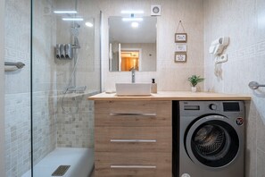 A bathroom with a glass shower enclosure, a sink with a mirror, a washing machine, and a hairdryer mounted on the wall. - Apartment 'Apartamentos Salou - 112' with Shared Pool, Wi-Fi and Air Conditioning (Salou)