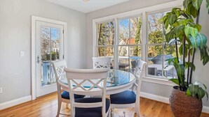 Un coin repas avec une table ronde en verre, des chaises blanches et une grande plante en pot.