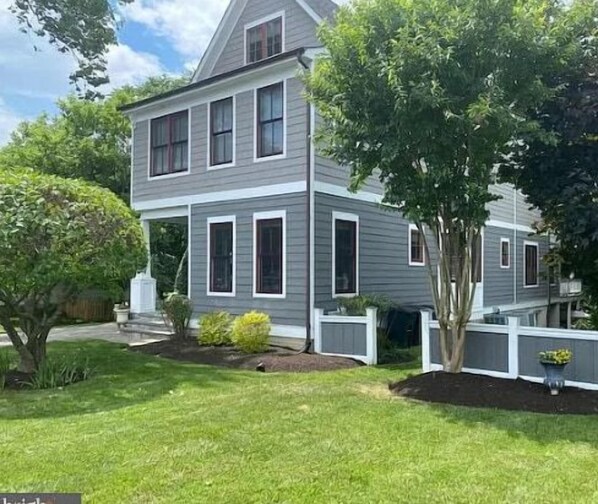 A two-story house with a front porch, a well-maintained lawn, and a tree in the yard.