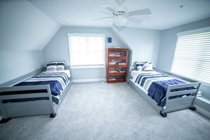 A bedroom with two single beds, a ceiling fan, a bookshelf, and a window with blinds.