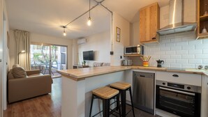 A modern kitchen with a built-in oven, a microwave, and a dishwasher. There is a wooden bar counter with stools and a large window providing natural light. - Apartment 'Salou - 111' with Shared Pool, Wi-Fi and Air Conditioning (Salou)