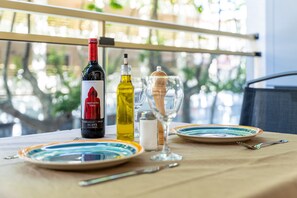 Una mesa con una botella de vino, una copa y platos, en un balcón con vistas a zonas verdes.