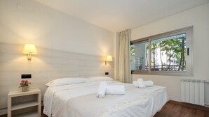 A hotel room with two beds, bedside lamps, a window with a view, and a radiator. - Apartment 'Salou - 111' with Shared Pool, Wi-Fi and Air Conditioning (Salou)
