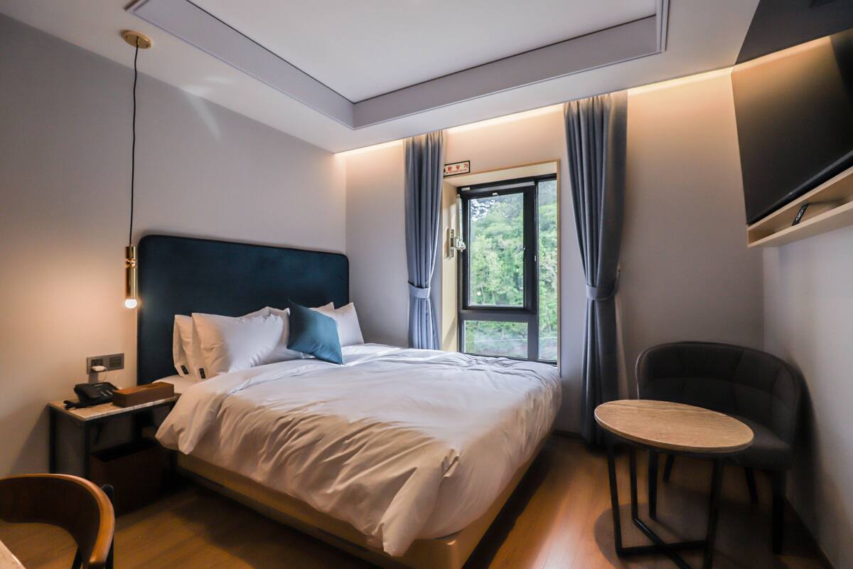 A modern hotel room with a bed, bedside table, chair, and a small table.