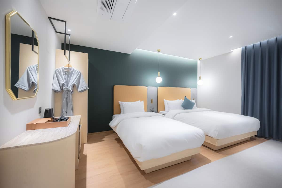 A modern hotel room with two beds, a vanity with a mirror, a robe, and a desk.