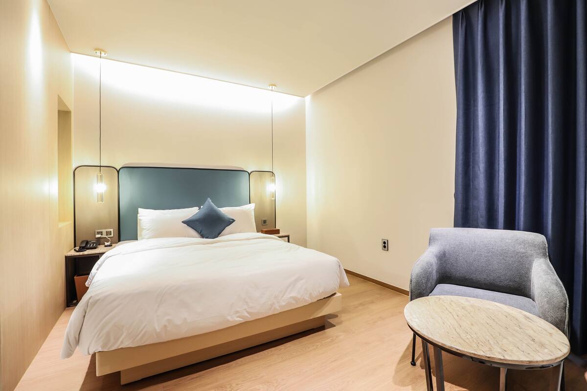 A modern hotel room with a large bed, bedside tables, a chair, and a small round table.