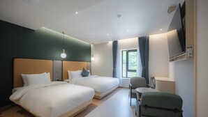 Ett hotellrum med två sängar, ett skrivbord, en stol, en tv och ett fönster med gardiner.
