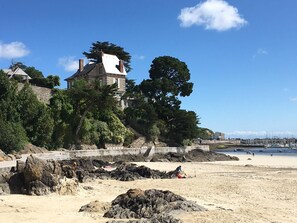 Ein Küstengebäude mit einer steinernen Fassade, umgeben von Bäumen und einem Sandstrand.