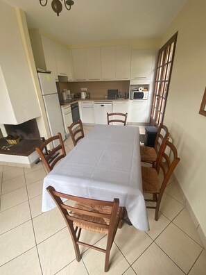 Une cuisine de taille modeste avec des meubles blancs, une table à manger recouverte d’une nappe blanche et des chaises en bois.