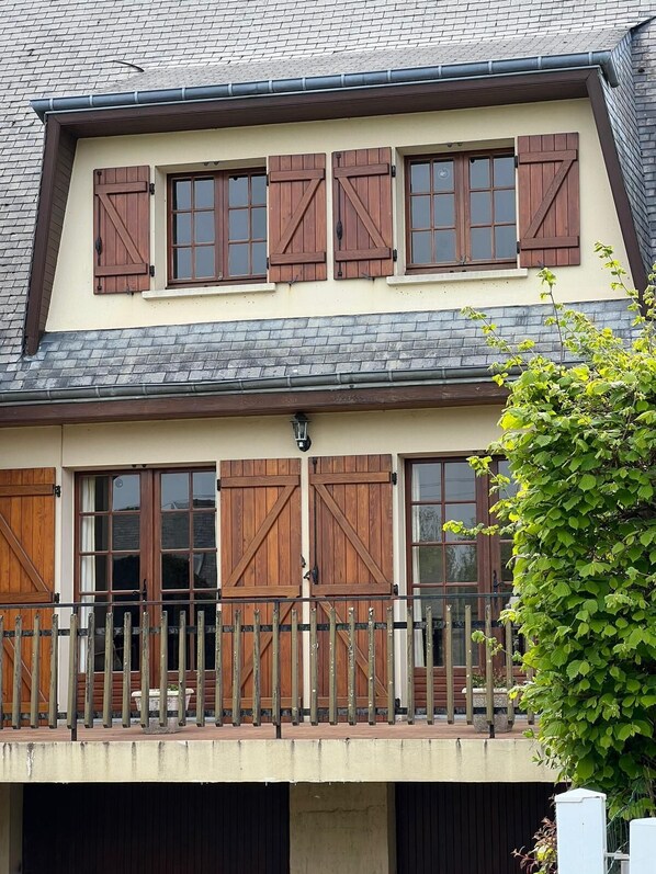 Un immeuble de deux étages doté d’un balcon et de volets en bois aux fenêtres.