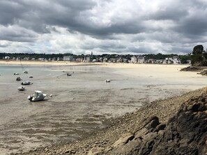 Une plage avec des bateaux, une rive sablonneuse et des bâtiments en arrière-plan.