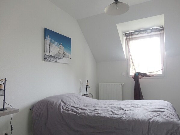 Une chambre à coucher avec un lit, un radiateur, une fenêtre avec des rideaux et un tableau accroché au mur.