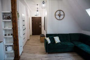 A modern living room with a green sectional sofa, a wooden floor, white built-in shelving, and a wooden door at the end of the hallway. - Apartament Uleczka (Torun)