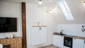 A modern kitchen with white cabinets, a wooden countertop, a built-in oven, and a large flat-screen TV. - Apartament Uleczka (Torun)