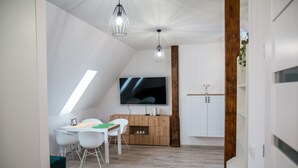A modern living room with a large flat-screen TV, a wooden cabinet, and a dining area with white chairs. - Apartament Uleczka (Torun)