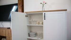 A white cabinet with shelves containing plates, glasses, and a vase with flowers. - Apartament Uleczka (Torun)