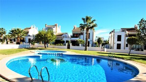 A swimming pool with a clear blue center, surrounded by a stone deck, with buildings in the background.